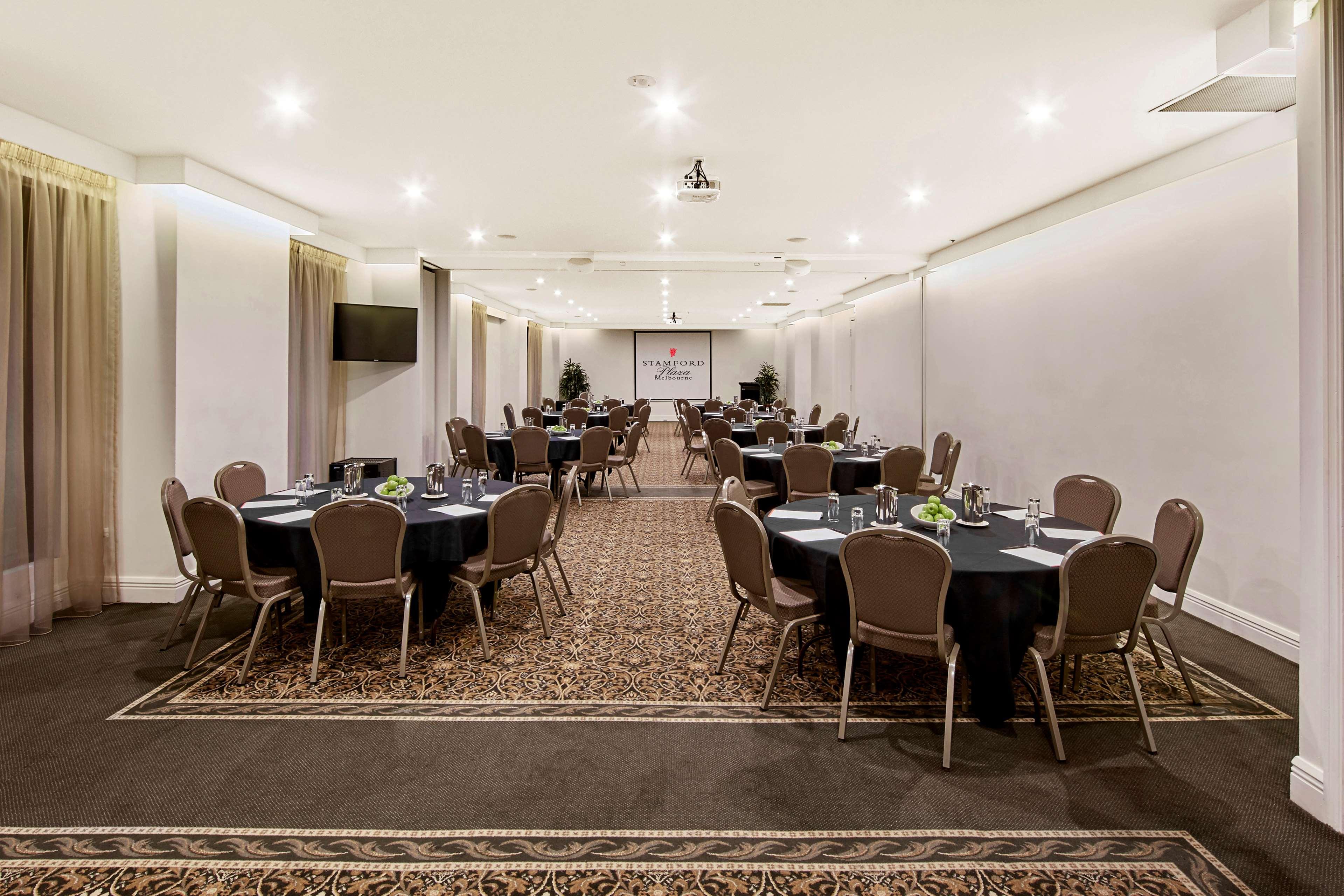 Stamford Plaza Melbourne Ξενοδοχείο Εξωτερικό φωτογραφία The photo shows an event space or banquet hall set up for a gathering. The room features several round tables covered with black tablecloths, each adorned with small centerpieces. Chairs are arranged around each table. The lighting is bright and mode