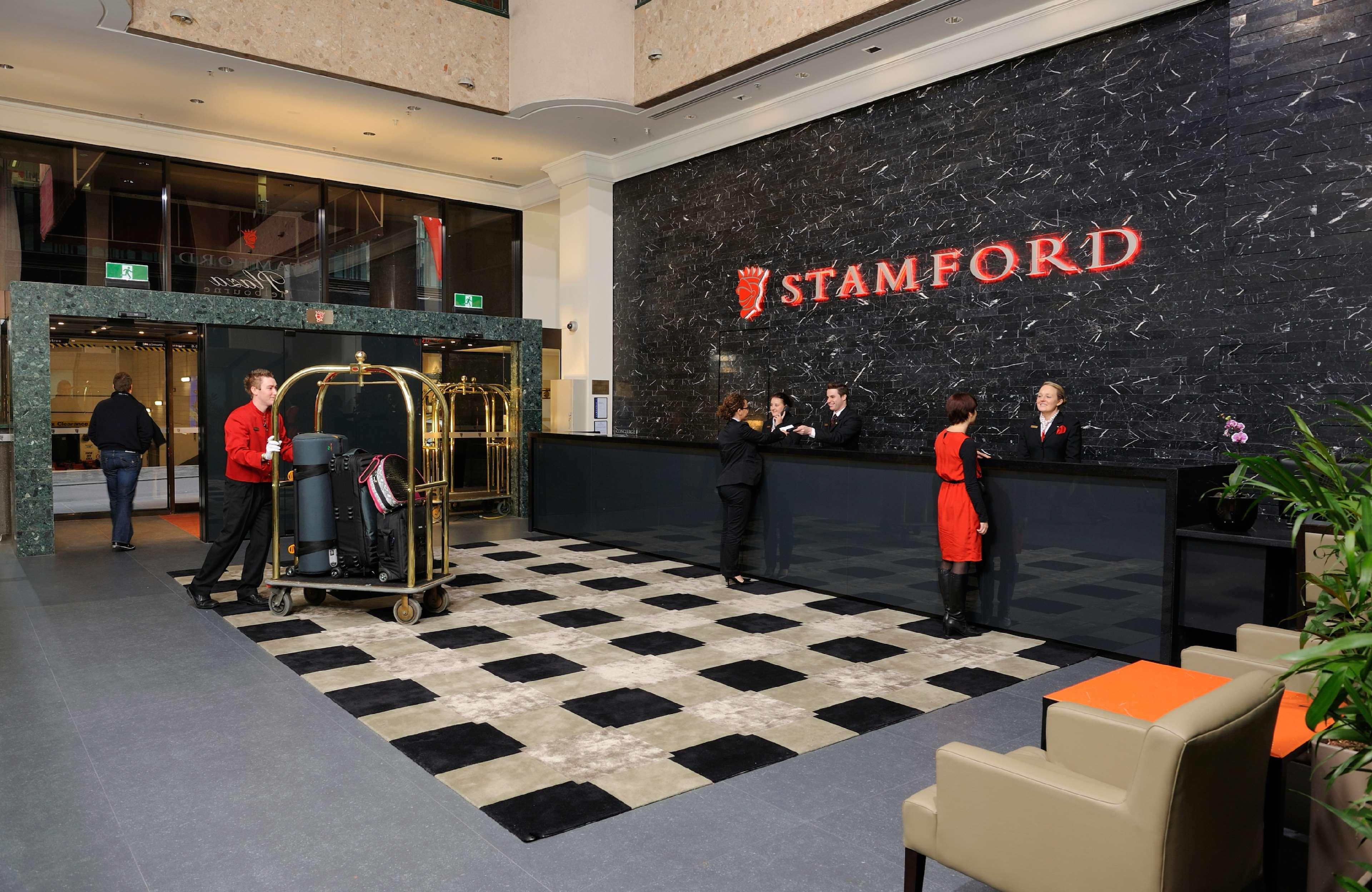 Stamford Plaza Melbourne Ξενοδοχείο Εσωτερικό φωτογραφία The photo shows the interior of a hotel lobby, specifically the Stamford Hotel. There is a large reception desk where several staff members are attending to guests. In the foreground, a bell cart loaded with luggage is positioned beside the reception