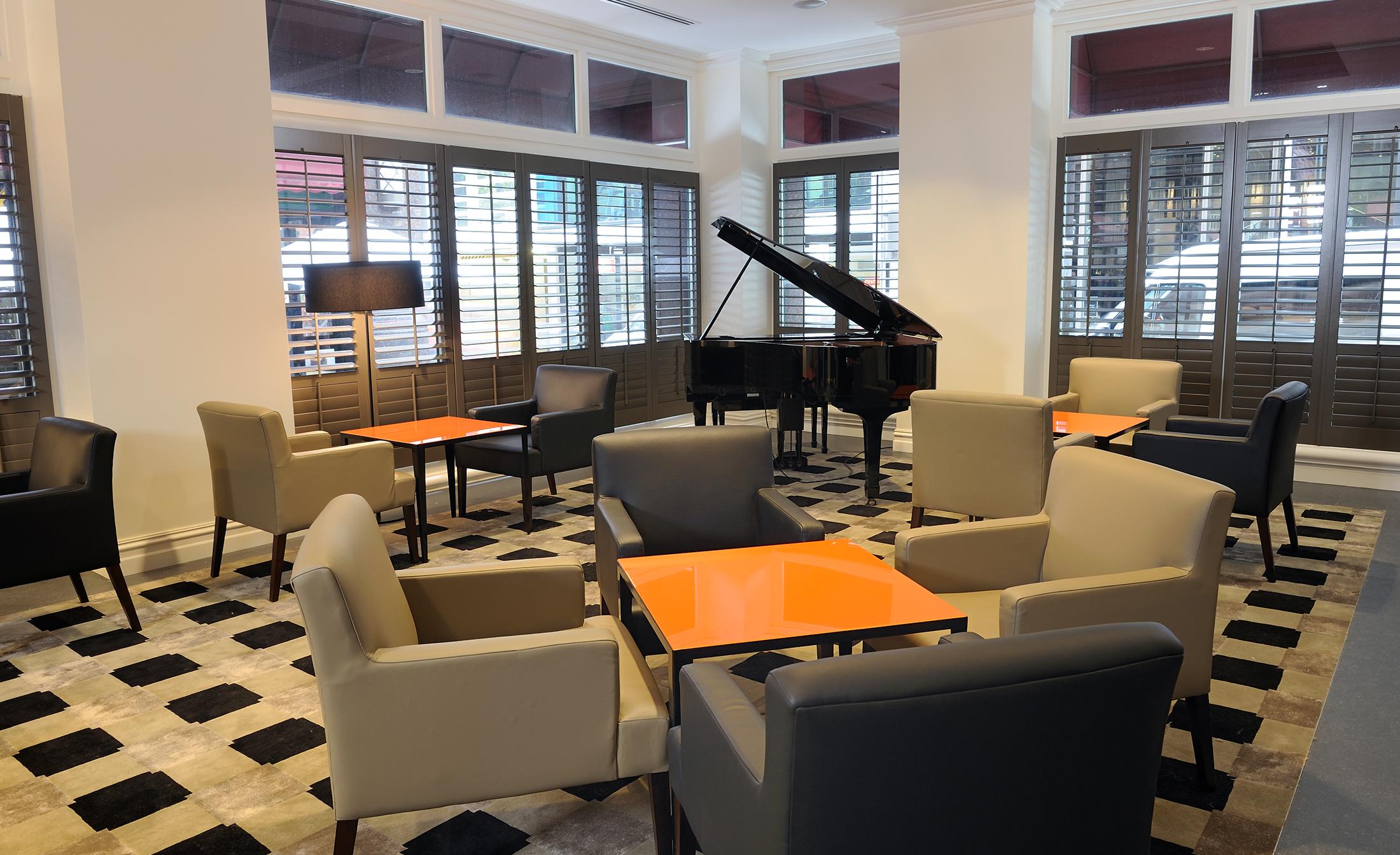 Stamford Plaza Melbourne Ξενοδοχείο Εξωτερικό φωτογραφία The photo shows a stylish indoor lounge area. It features several light gray armchairs arranged around orange square tables. In the corner, there is a black grand piano, adding an elegant touch to the space. The room has large windows with wooden shu