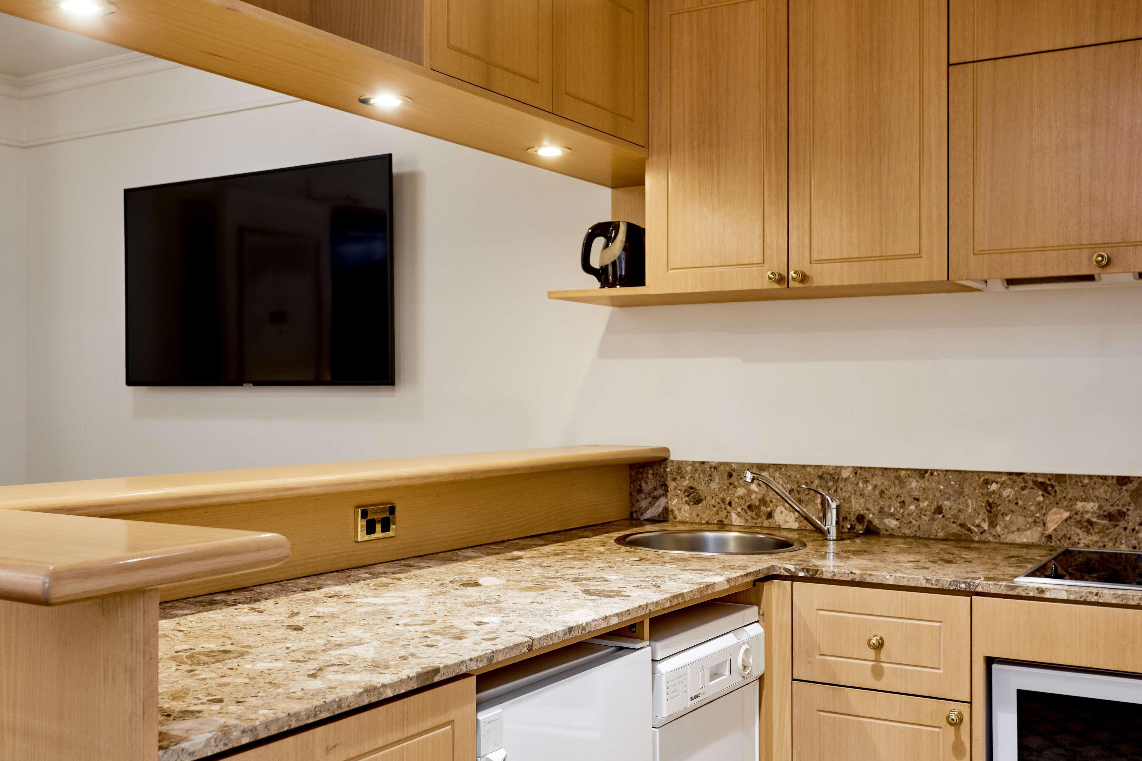 Stamford Plaza Melbourne Ξενοδοχείο Εξωτερικό φωτογραφία The photo shows a modern kitchen with wooden cabinetry and a granite countertop. There's a stainless steel sink integrated into the countertop, and appliances including a dishwasher and possibly a coffee maker on the shelf above. A flat-screen televi