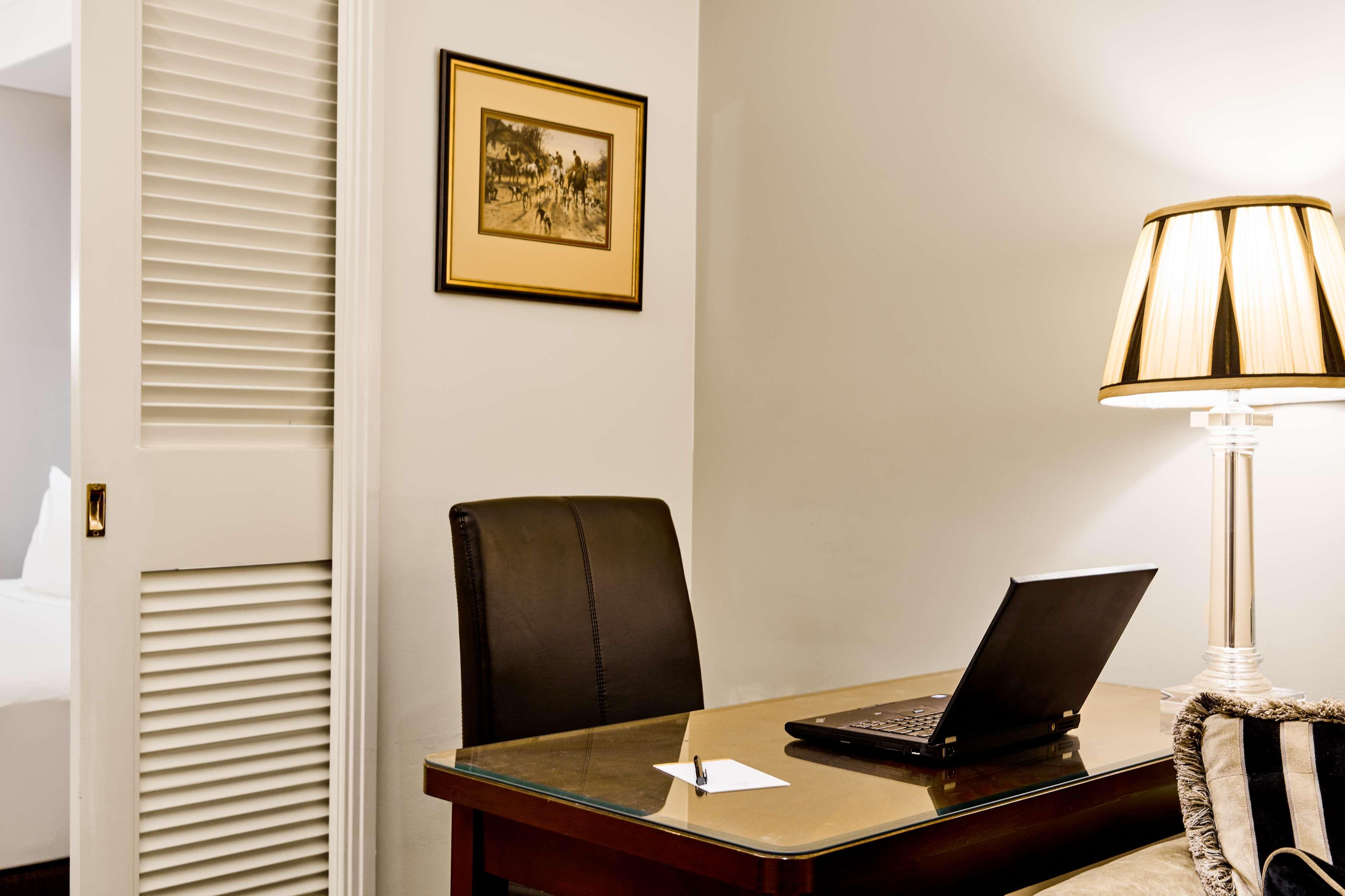 Stamford Plaza Melbourne Ξενοδοχείο Εξωτερικό φωτογραφία The photo shows a small office or workspace. There is a desk with a glass surface, and on it sits a laptop computer. A piece of paper or notecard is also placed on the desk. Behind the desk is a black office chair. A wall lamp with a striped shade is