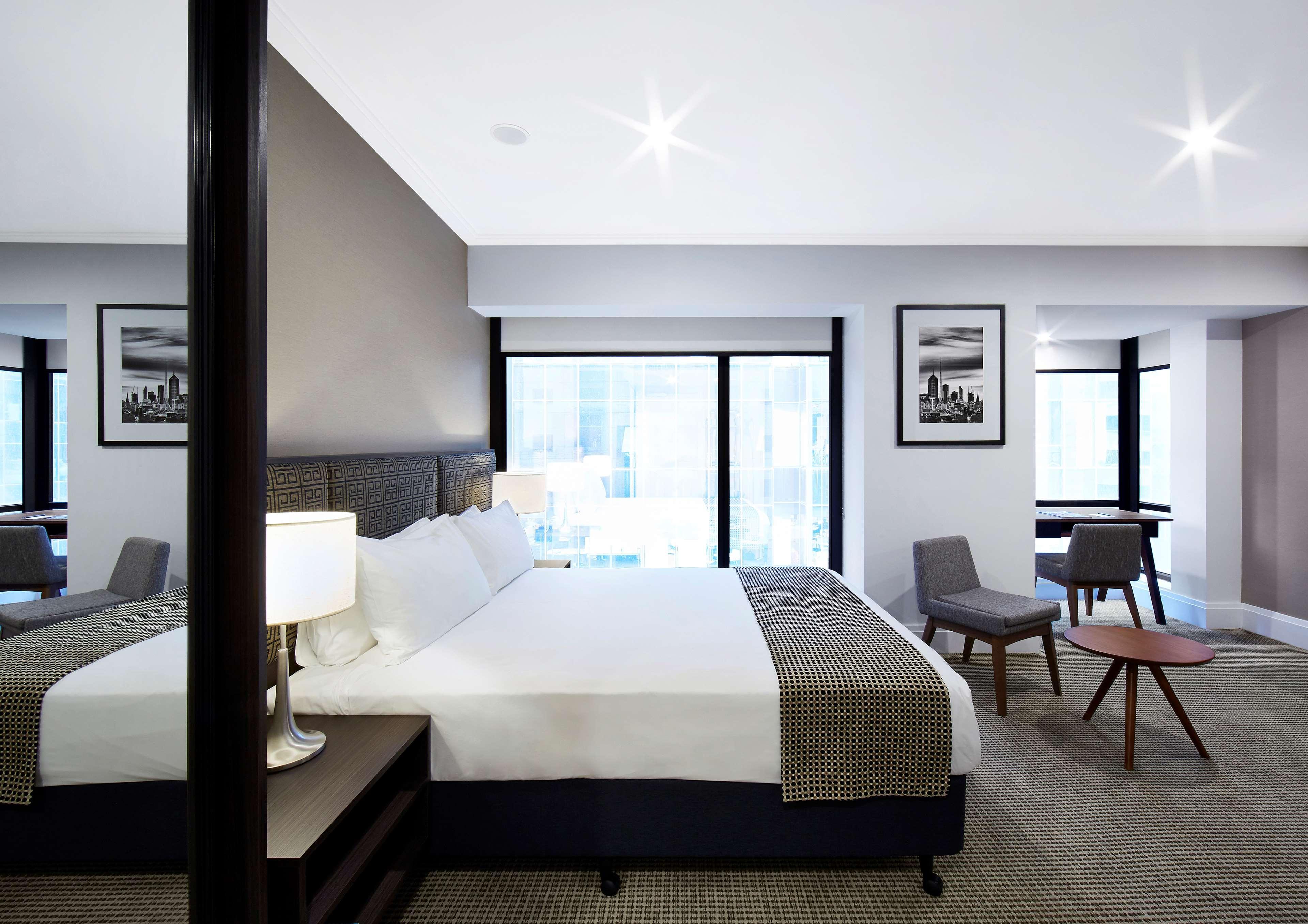 Stamford Plaza Melbourne Ξενοδοχείο Εξωτερικό φωτογραφία The image shows a modern hotel room featuring a large bed with white linens and a gray throw blanket. There are two windows that allow natural light to enter the space, and the walls are painted in a light color. In addition to the bed, there are two