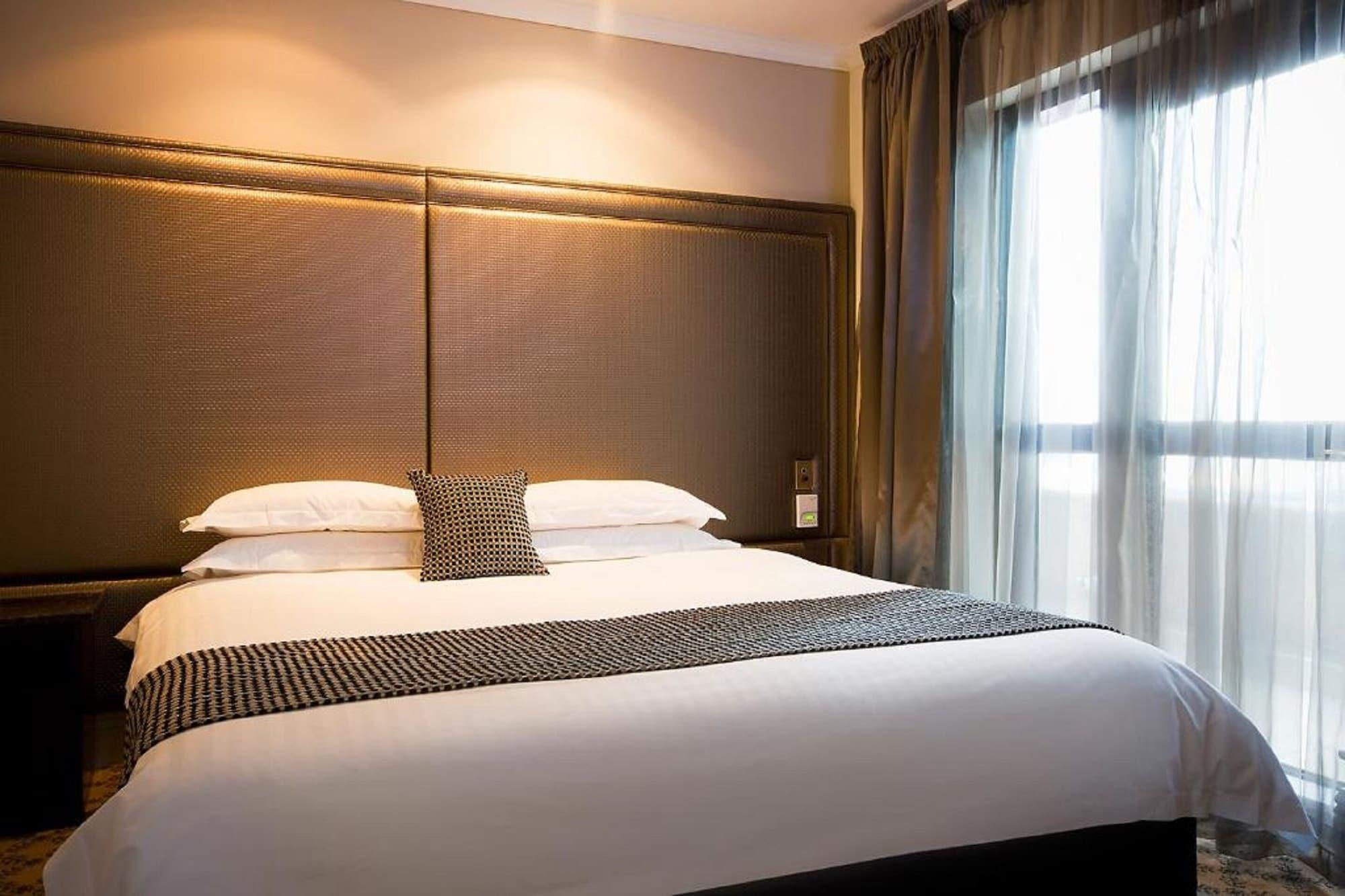Stamford Plaza Melbourne Ξενοδοχείο Εξωτερικό φωτογραφία The photo shows a modern bedroom featuring a large bed with a neatly arranged white comforter and decorative pillows. The headboard is upholstered in a dark material, and there is soft lighting above it. On one side of the bed, there’s a small decora