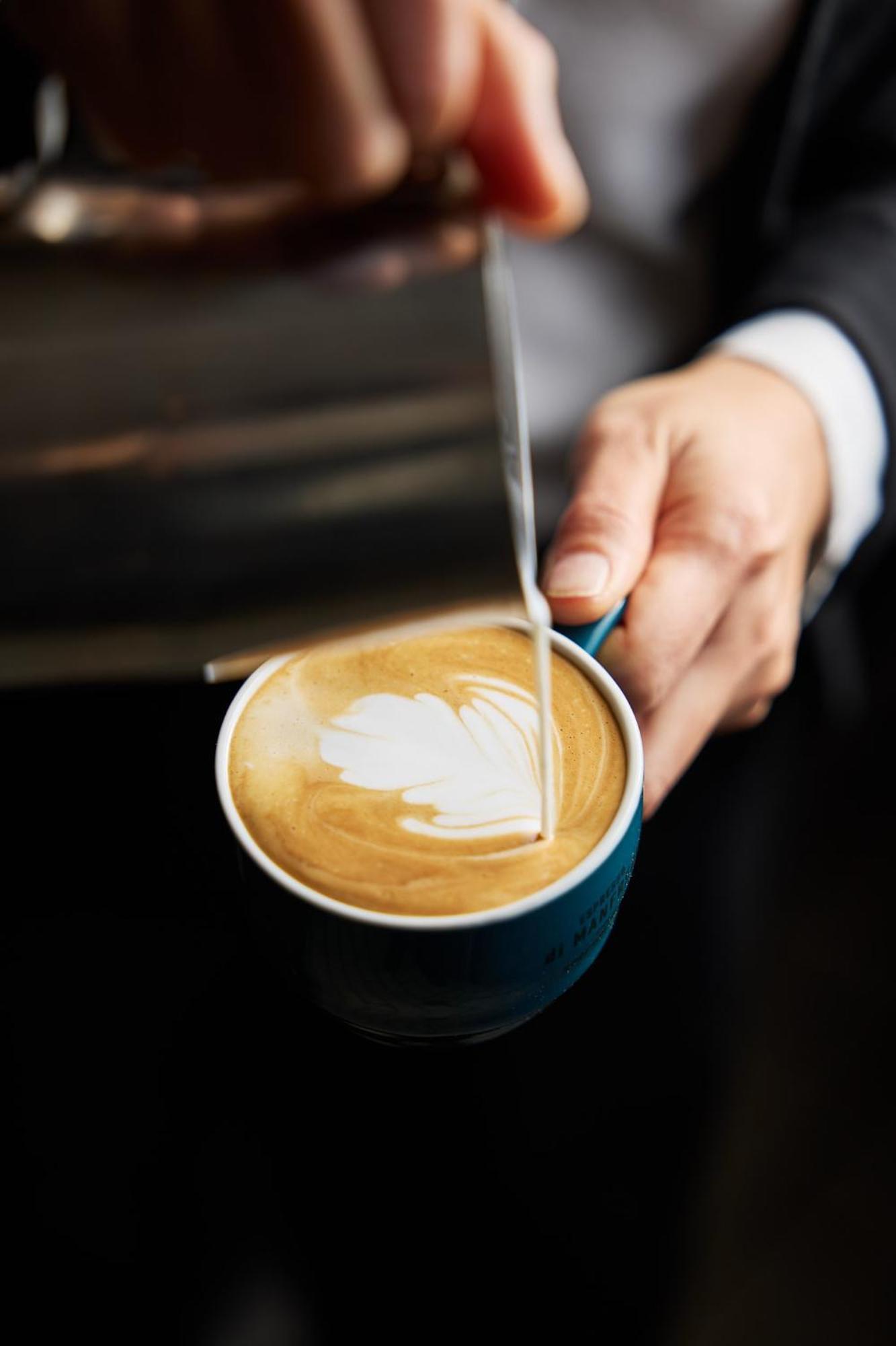 Stamford Plaza Melbourne Ξενοδοχείο Εξωτερικό φωτογραφία The photo shows a close-up of a hand holding a cup of coffee with a latte art design on the surface. The coffee appears to be a creamy, caramel color, likely a latte or cappuccino. A small stream of milk is being poured into the cup, creating a heart