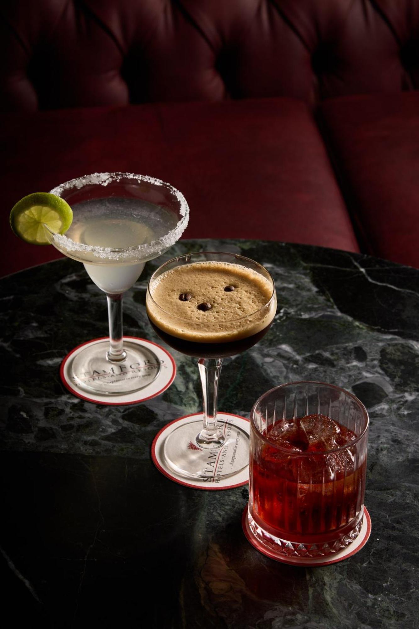 Stamford Plaza Melbourne Ξενοδοχείο Εξωτερικό φωτογραφία The photo displays three different cocktails arranged on a dark marble table. 

1. On the left, there is a margarita glass filled with a clear drink, garnished with a lime slice and featuring a salted rim.
2. In the center, a coupe glass holds a dark