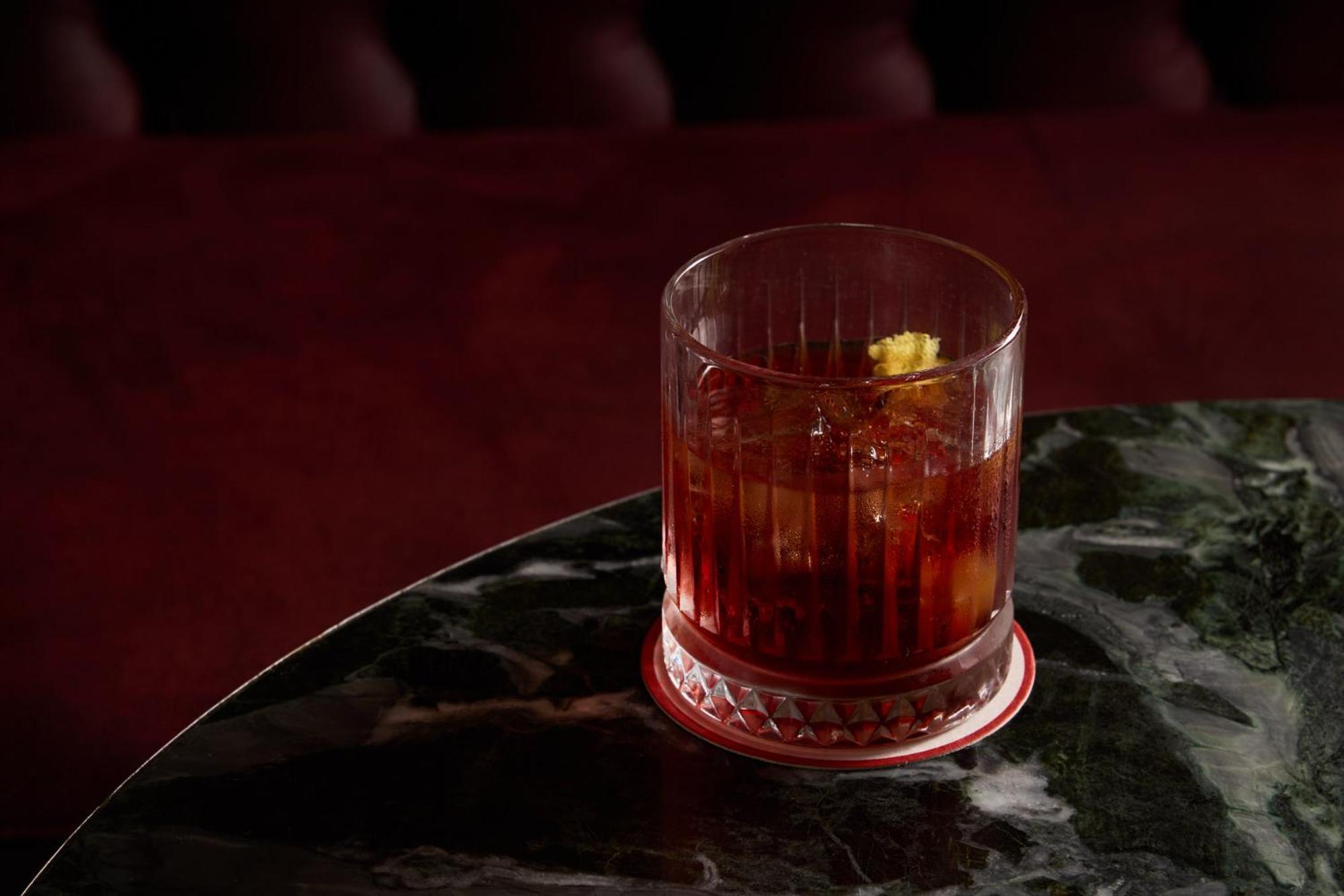 Stamford Plaza Melbourne Ξενοδοχείο Εξωτερικό φωτογραφία The photo depicts a short glass filled with a dark-colored beverage, likely an alcoholic drink. The glass has a textured design, with ice cubes visible inside. A twist of lemon peel is perched on the rim, adding a touch of garnish. The drink sits on 