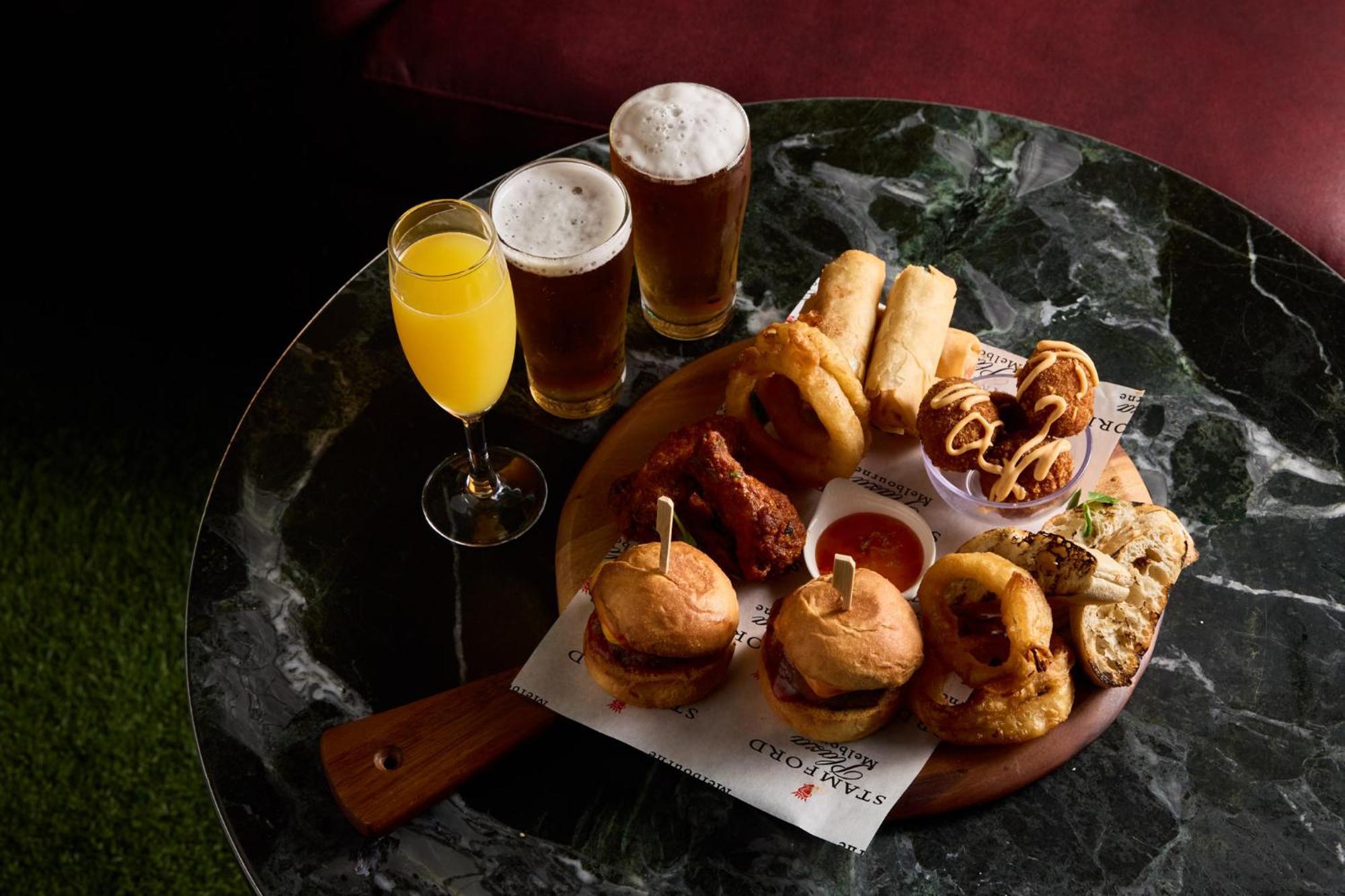 Stamford Plaza Melbourne Ξενοδοχείο Εξωτερικό φωτογραφία The photo displays a variety of food and drinks arranged on a marble table. There are small burgers garnished with skewers, crispy chicken pieces, and deep-fried snacks. Additionally, there are two glasses of beer and a cocktail, likely a mimosa, pre