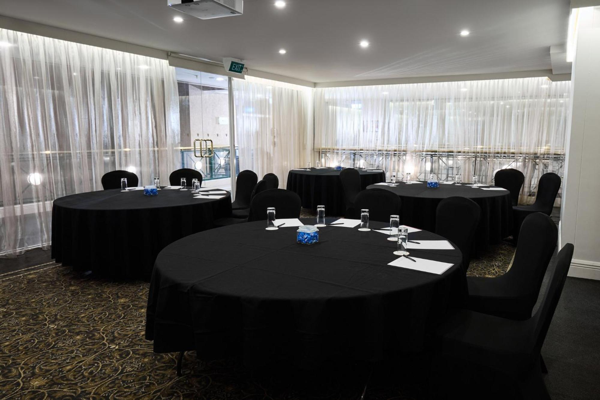 Stamford Plaza Melbourne Ξενοδοχείο Εξωτερικό φωτογραφία The photo shows a meeting or conference room set up with several round tables covered in black tablecloths. Each table is accompanied by black chairs. There are some white notepads and pens placed on the tables, and a small decorative item, possibly 